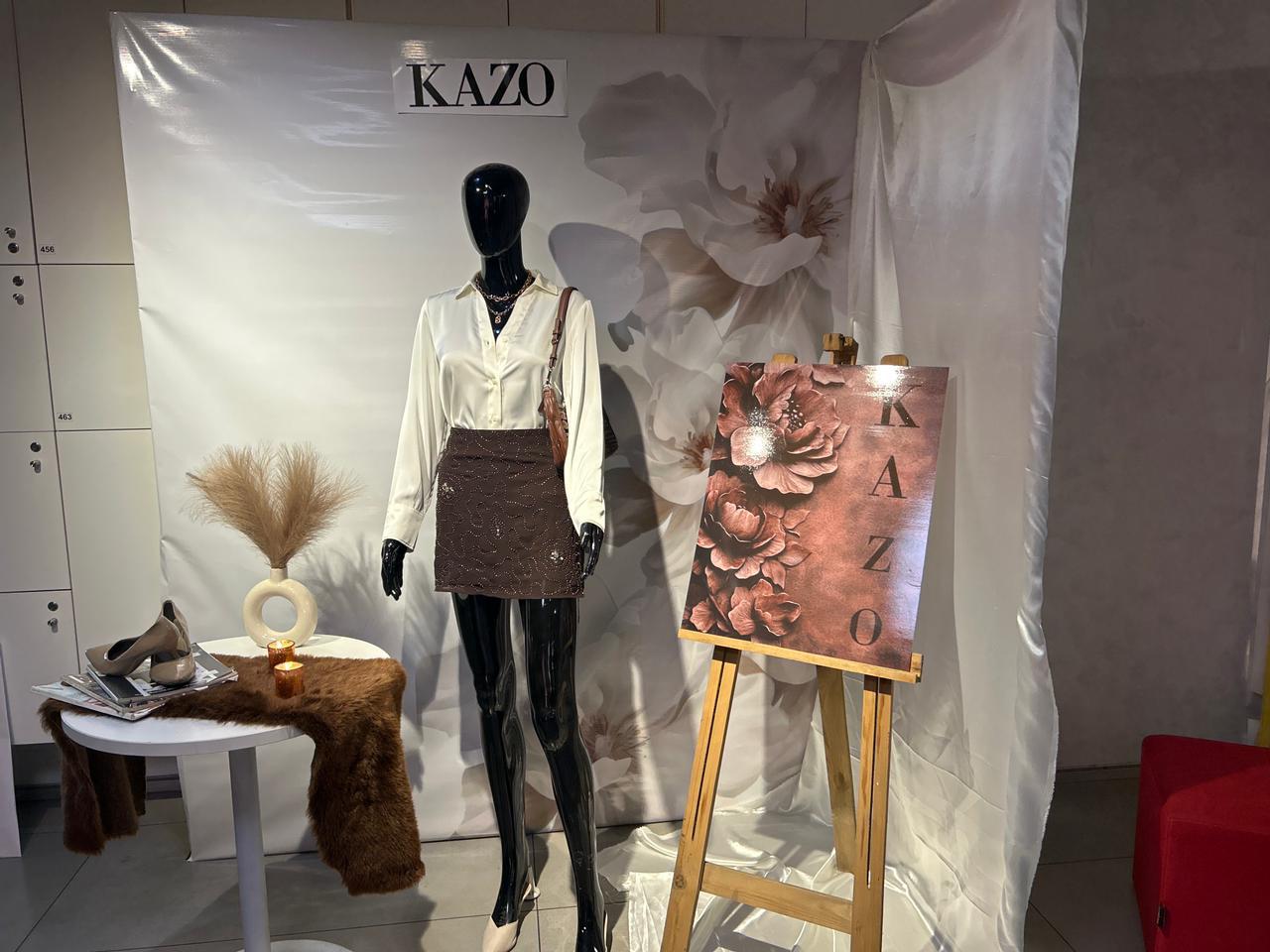Kazo retail window installation with a mannequin styled in an ivory shirt and brown embellished skirt beside a copper floral Kazo board.